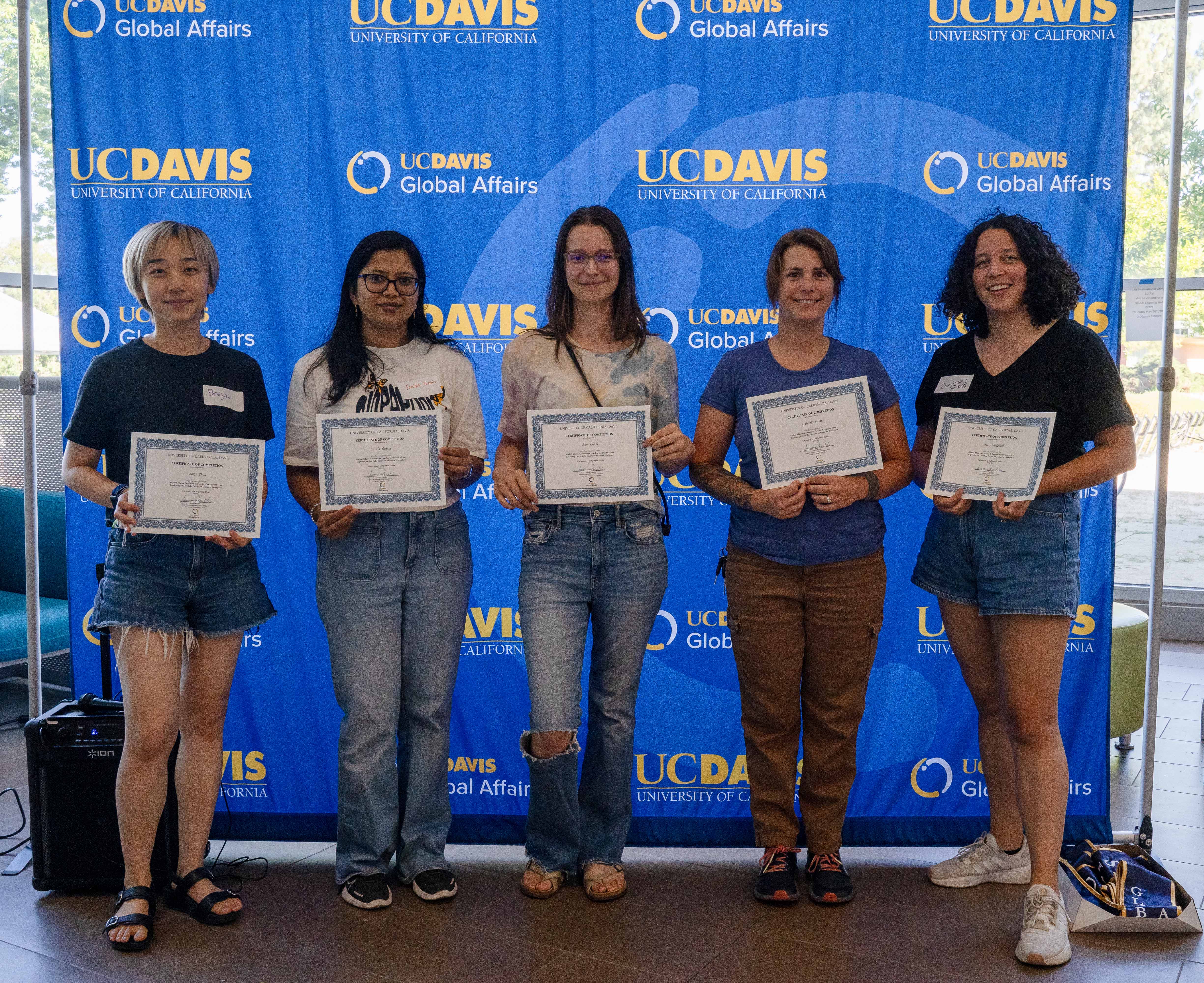 Five students holding certificates stand in front of a UC Davis Global Affairs backdrop.