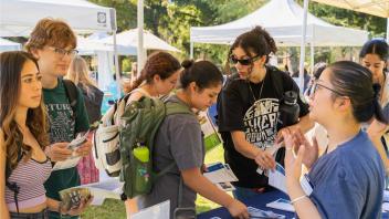 Photo of students gathered around a tabling getting information about global learning opportunities. They are outdoor at the Global Learning Fair on the UC Davis campus.