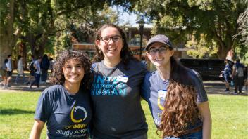 photo of three staff members looking at the camera, smiling. They are attending the outdoor Global Learning Fair at UC Davis.