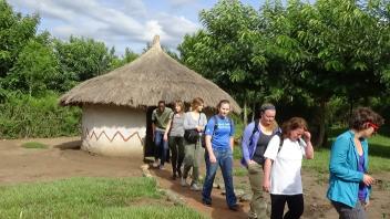 A group photos with a hut structure in the background.