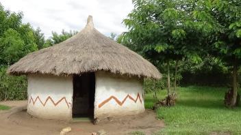 A hut structure standing alone in a grassy area with trees surrounding it