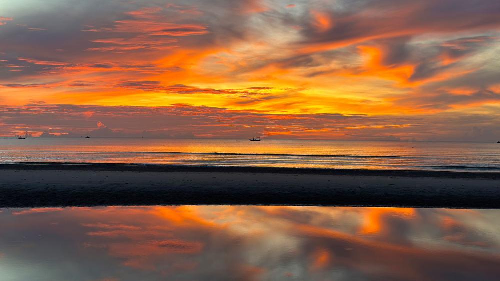 Photo of a sunrise. Boats can been seen out in the distance.