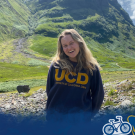 UC Davis student Anya Nygaard smiles at the camera wearing a UCD sweatshirt with the Scottish Highlands in the background. A blue watercolor overlay with Global Aggies is over the bottom of the photo.