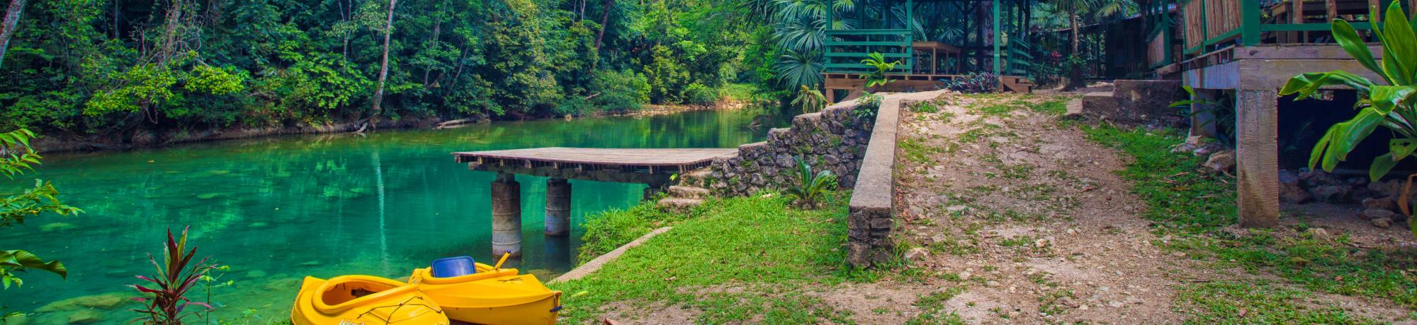 photo of a stream in Belize with yellow paddle boats parked along the side.