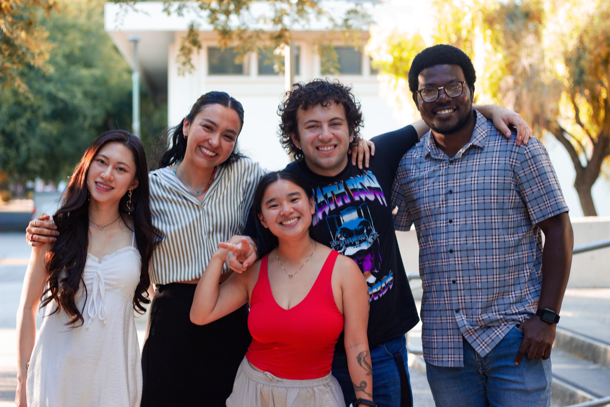 A group of five diverse friends smiling together outdoors in casual clothing.