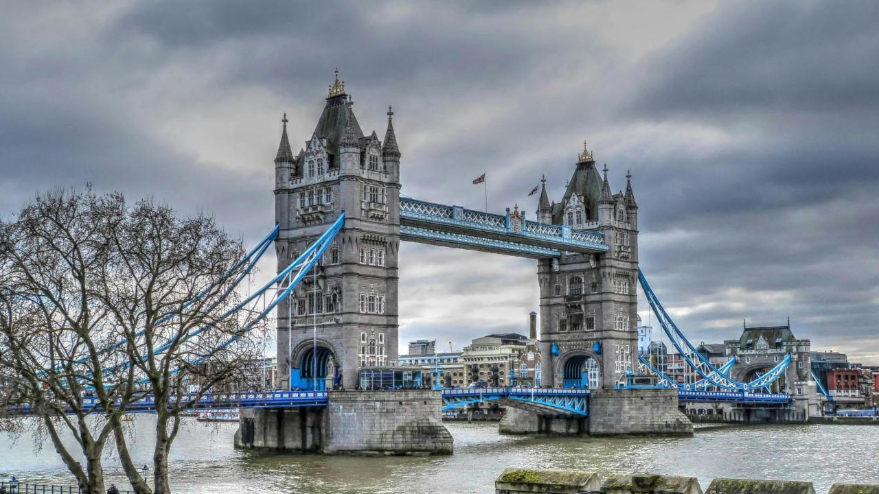 Tower Bridge in London with overcast skies and the River Thames flowing below.