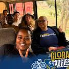 Group of smiling UC Davis students and partners posing on a bus, flashing peace signs and thumbs up.