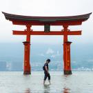 A man stands in calm water, reflecting the serene surroundings and the clear sky above.
