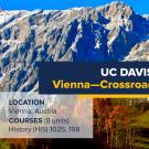 Promotional banner for the UC Davis Summer Abroad program titled 'Vienna—Crossroads of Central Europe.' In the foreground, a scenic alpine church with a traditional red-roofed bell tower stands on a grassy hillside, surrounded by autumn trees. In the background, a striking mountain range with rugged, rocky peaks rises against a bright blue sky. Text overlays include program details: 'Location: Vienna, Austria,' and 'Courses: (8 units) History (HIS) 102S, 198.' A logo is in the right bottom corner.