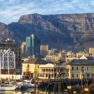 Waterfront with boats and colorful buildings, set against a large, flat-topped mountain range.