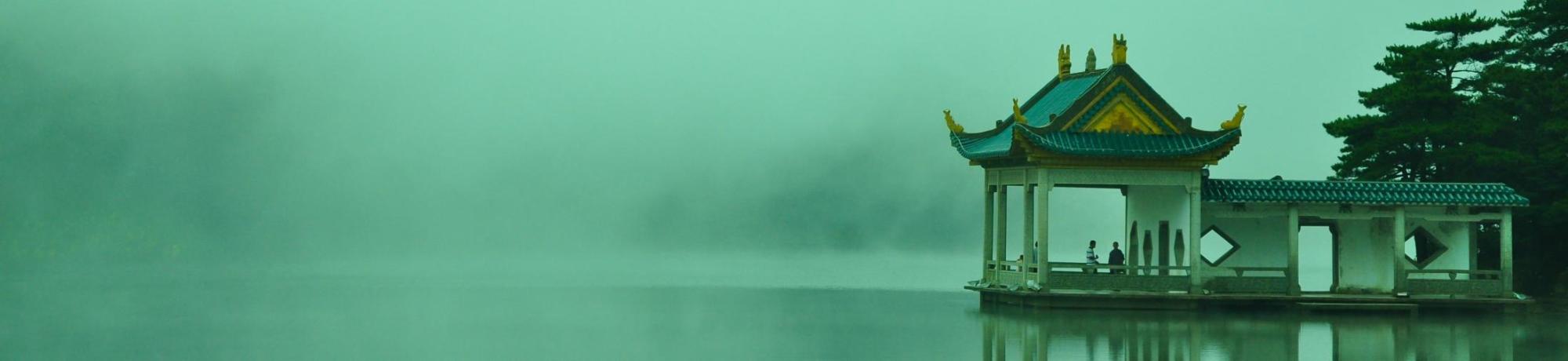 Serene waterside pavilion shrouded in mist, surrounded by soft green hues.
