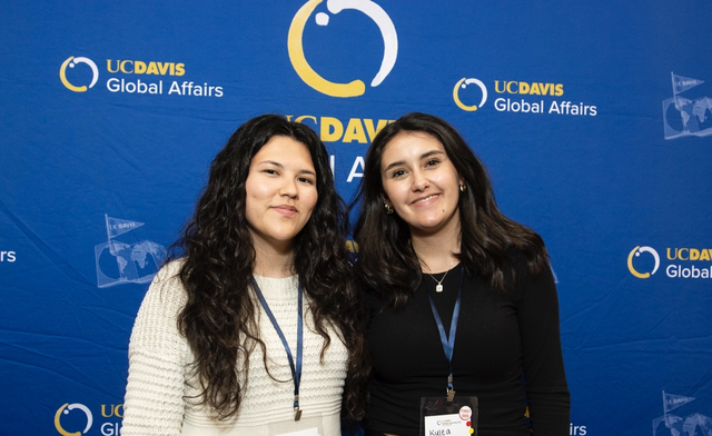 Two smiling women standing before UC Davis Global Affairs blue backdrop