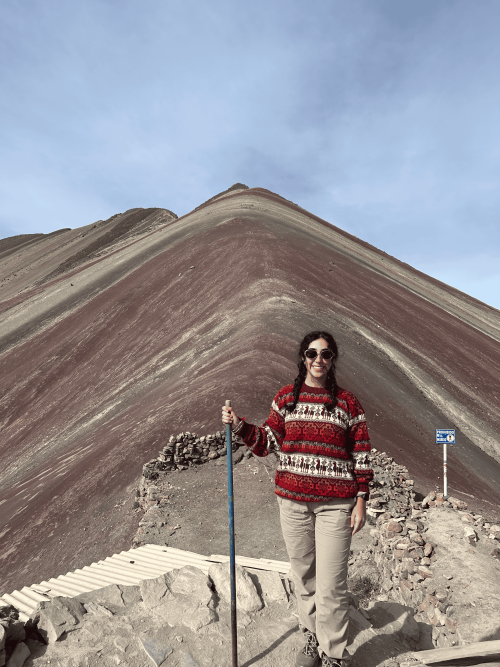 Hiker holding pole in red sweater and sunglasses on Rainbow Mountain's striped slopes