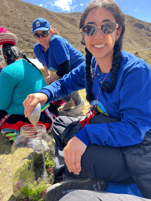 Smiling woman in blue sunglasses on mountain slope holding a jar with plants