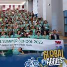Group of participants in turquoise shirts posing with a banner for Climate Corps Summer School 2025