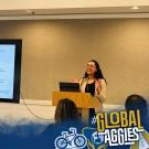A speaker presents at a podium with a slide in Spanish displayed on a screen behind them and an audience seated in front. UC Davis Global Affairs and #GlobalAggies logos appears in the bottom corners.