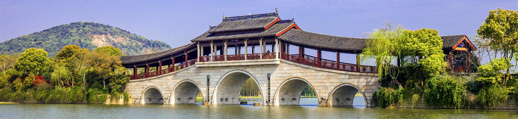 Traditional arched bridge over a tranquil lake, surrounded by lush greenery and hills.