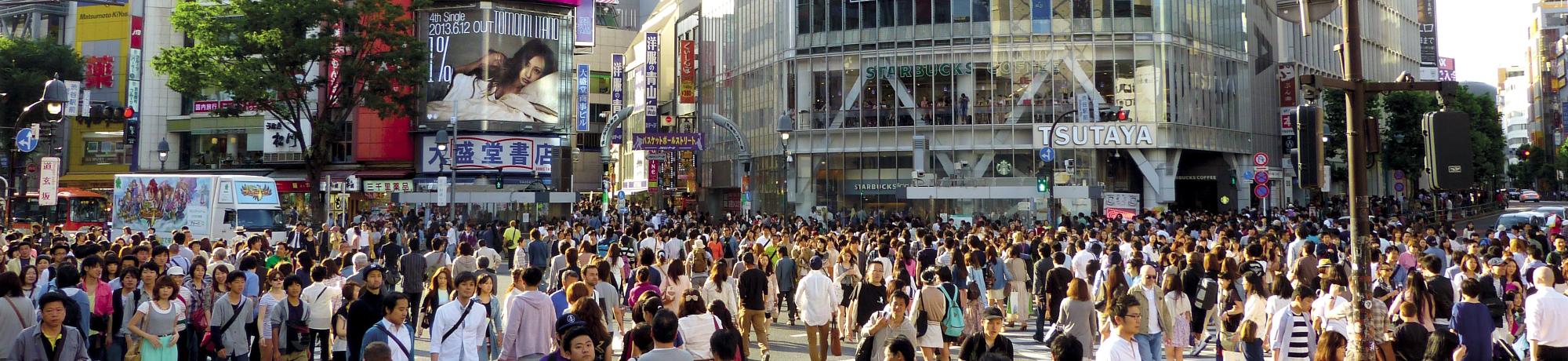 Bustling urban intersection filled with pedestrians, surrounded by colorful billboards.